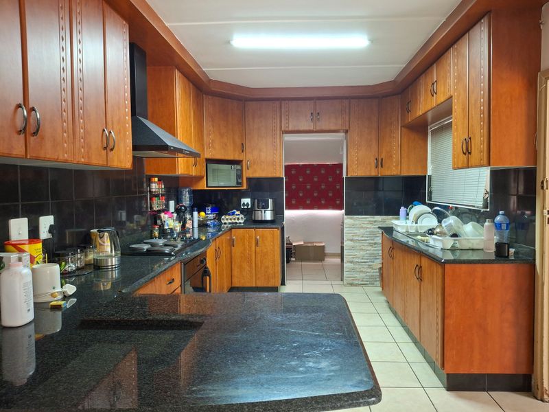 A functional kitchen featuring extensive wooden cabinetry, granite countertops, a built-in oven, hob, and extractor fan with a tiled backsplash.
