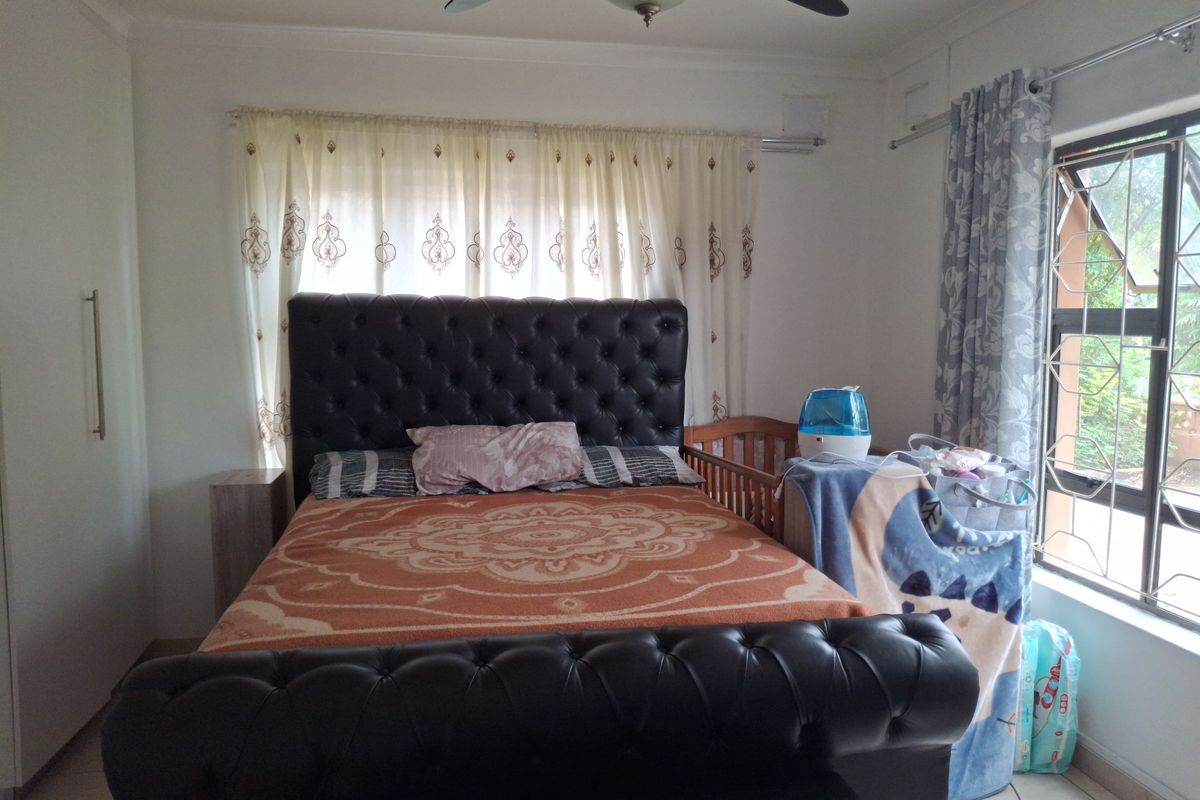 A functional bedroom featuring tiled flooring, a ceiling fan, and built-in wardrobe storage with security bars on the windows.