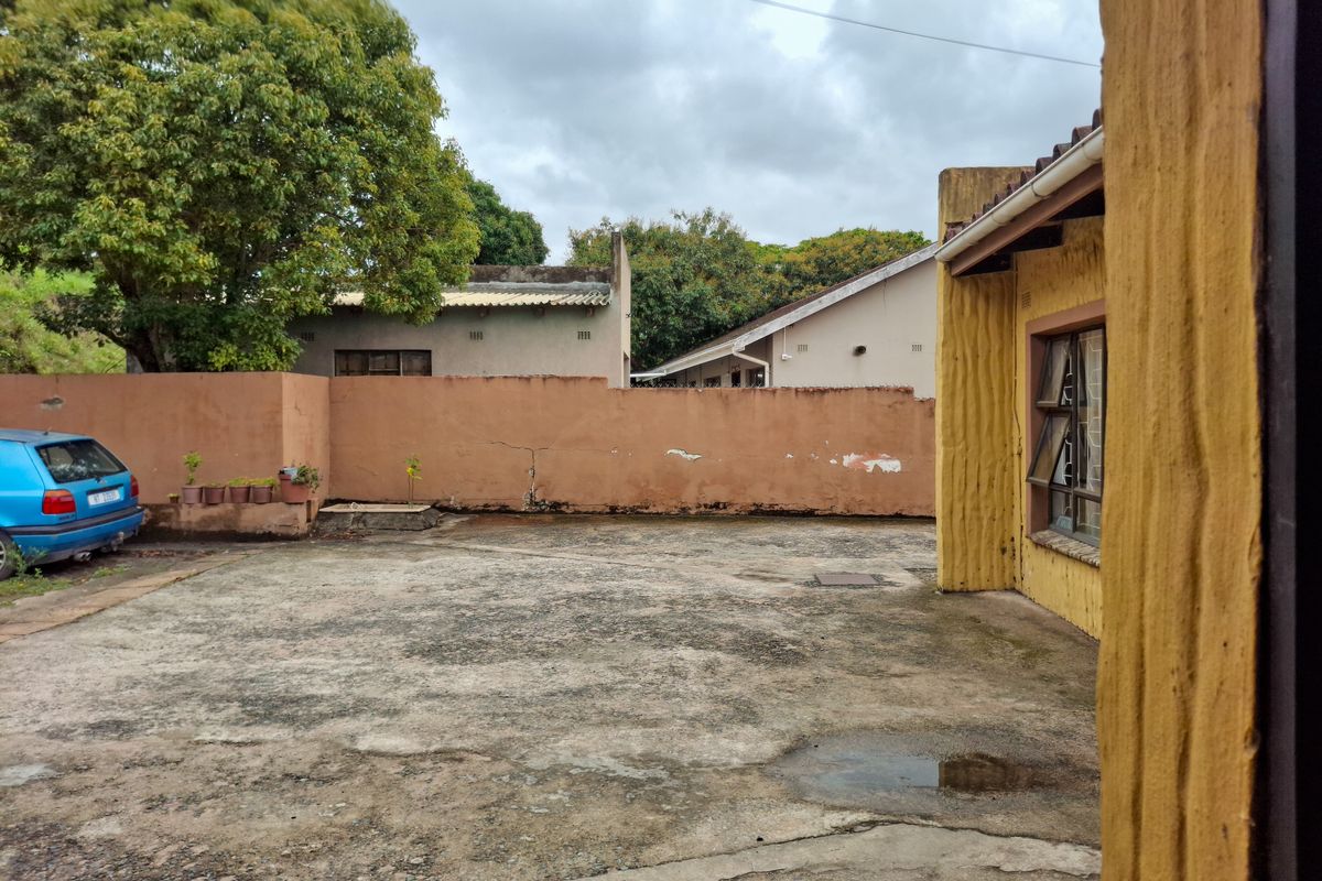 A rear exterior view showing a concrete driveway area, boundary wall with visible wear, and the side elevation of the house.