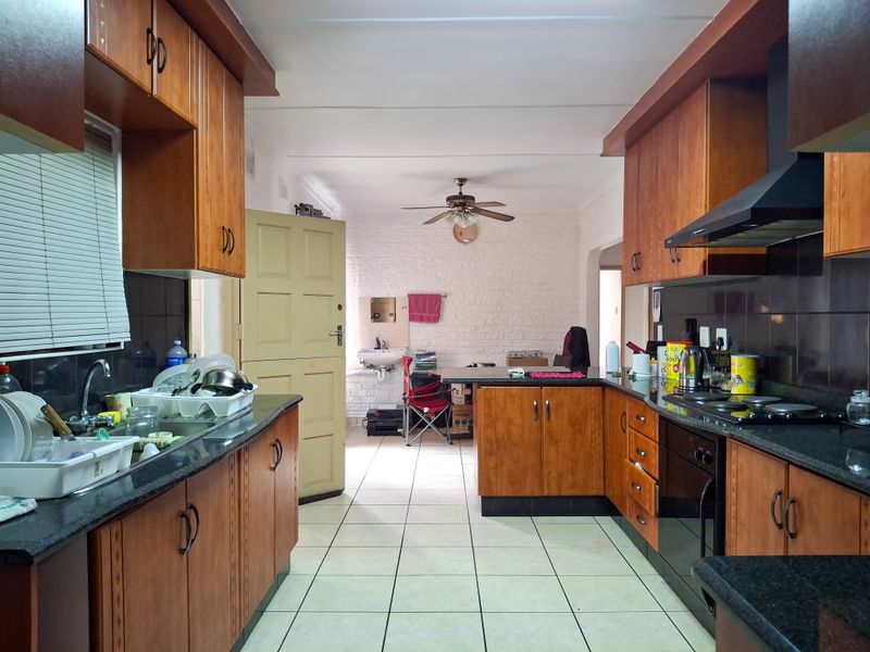 A functional kitchen featuring wooden cabinetry, granite countertops, built-in oven, and hob, with tiled flooring and a ceiling fan.