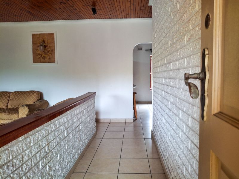 A hallway featuring tiled flooring, an exposed brick wall, and a timber ceiling, leading through an archway into an adjacent living space.