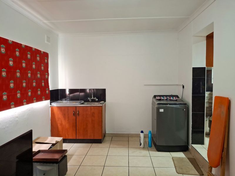 A functional laundry area featuring tiled flooring, a built-in sink with laminate cabinetry, and a tiled splashback.