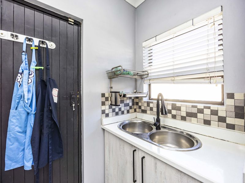 A functional scullery area featuring a double bowl stainless steel sink, modern black mixer tap, tiled splashback, and built-in cabinetry.