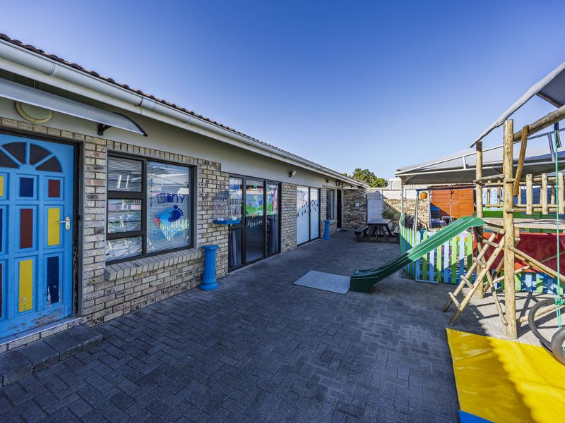 A paved rear courtyard area featuring a face brick facade, sliding glass door access, and a covered outdoor play structure.