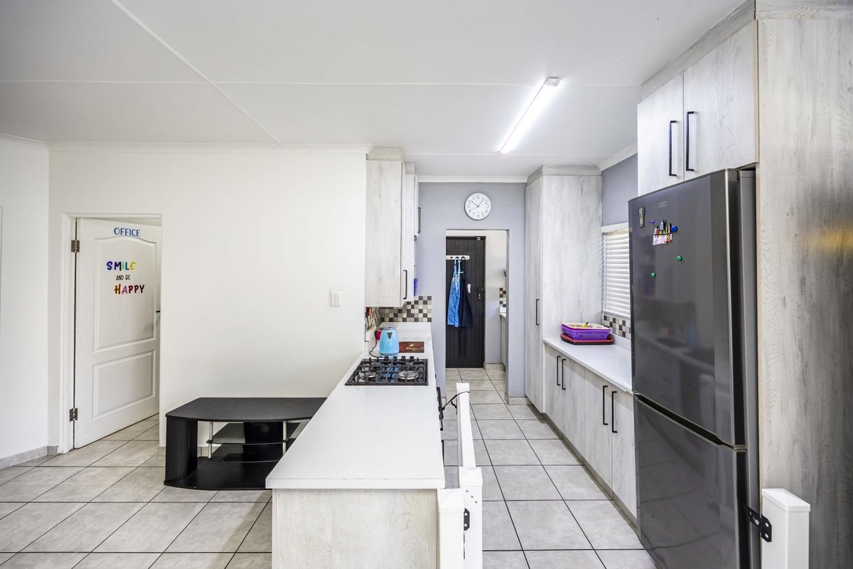 A functional kitchen featuring light-toned cabinetry, tiled flooring, a gas hob, and ample counter space, leading through to a secondary utility area.