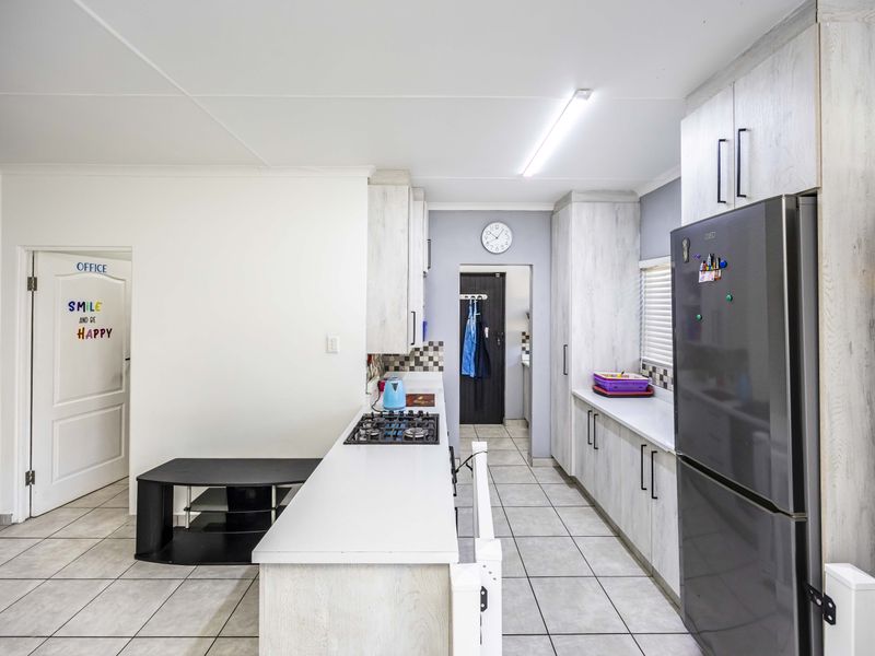 A functional kitchen featuring light-toned cabinetry, tiled flooring, a gas hob, and ample counter space, leading through to a secondary utility area.