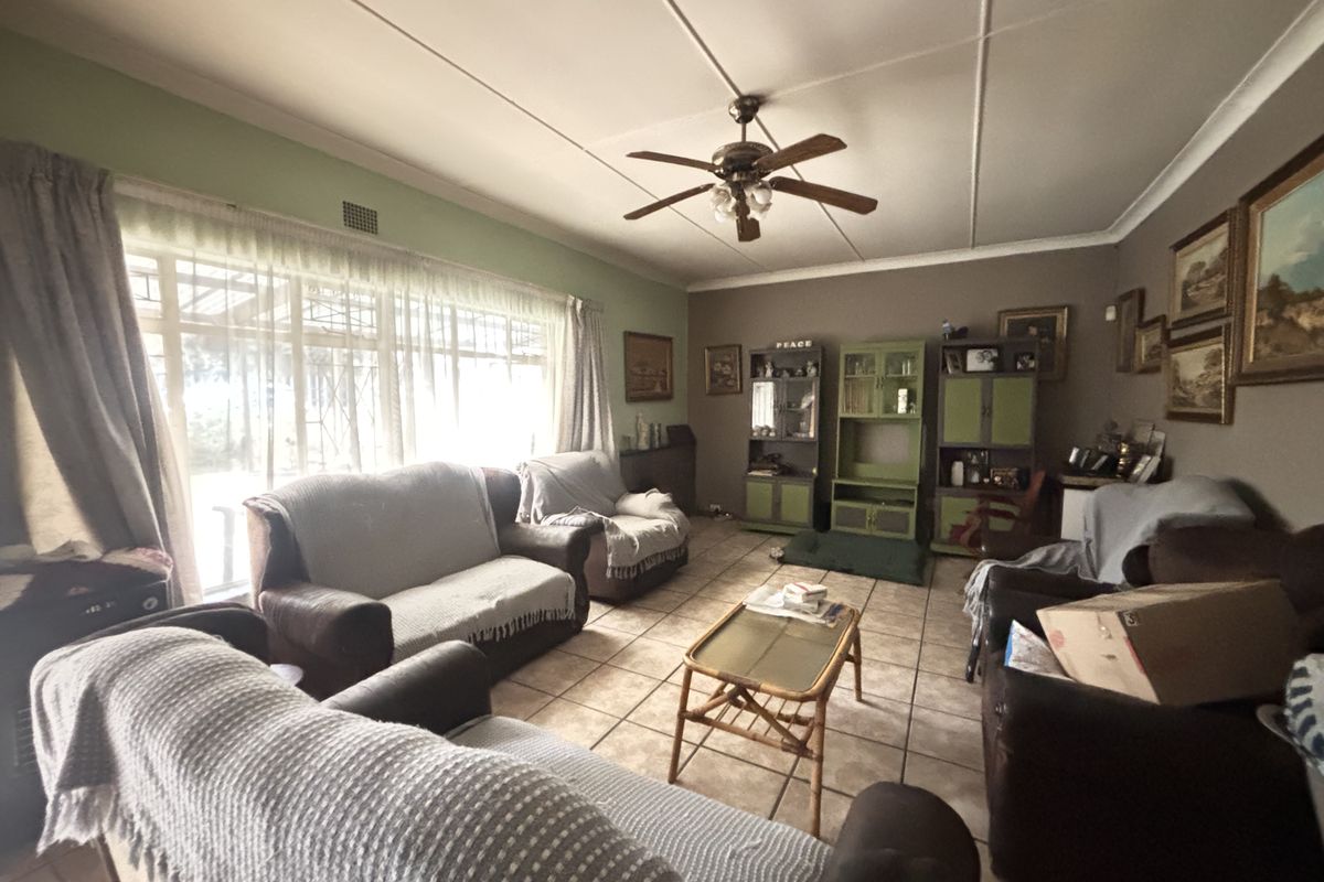 A spacious living room featuring tiled flooring, a ceiling fan, and large windows that provide ample natural light.