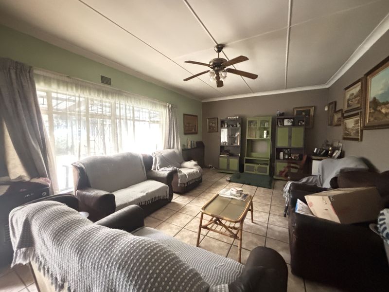 A spacious living room featuring tiled flooring, a ceiling fan, and large windows that provide ample natural light.