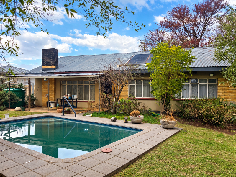 Rear view of the house featuring a swimming pool, tiled pool deck, solar water heating system, and a brick chimney.