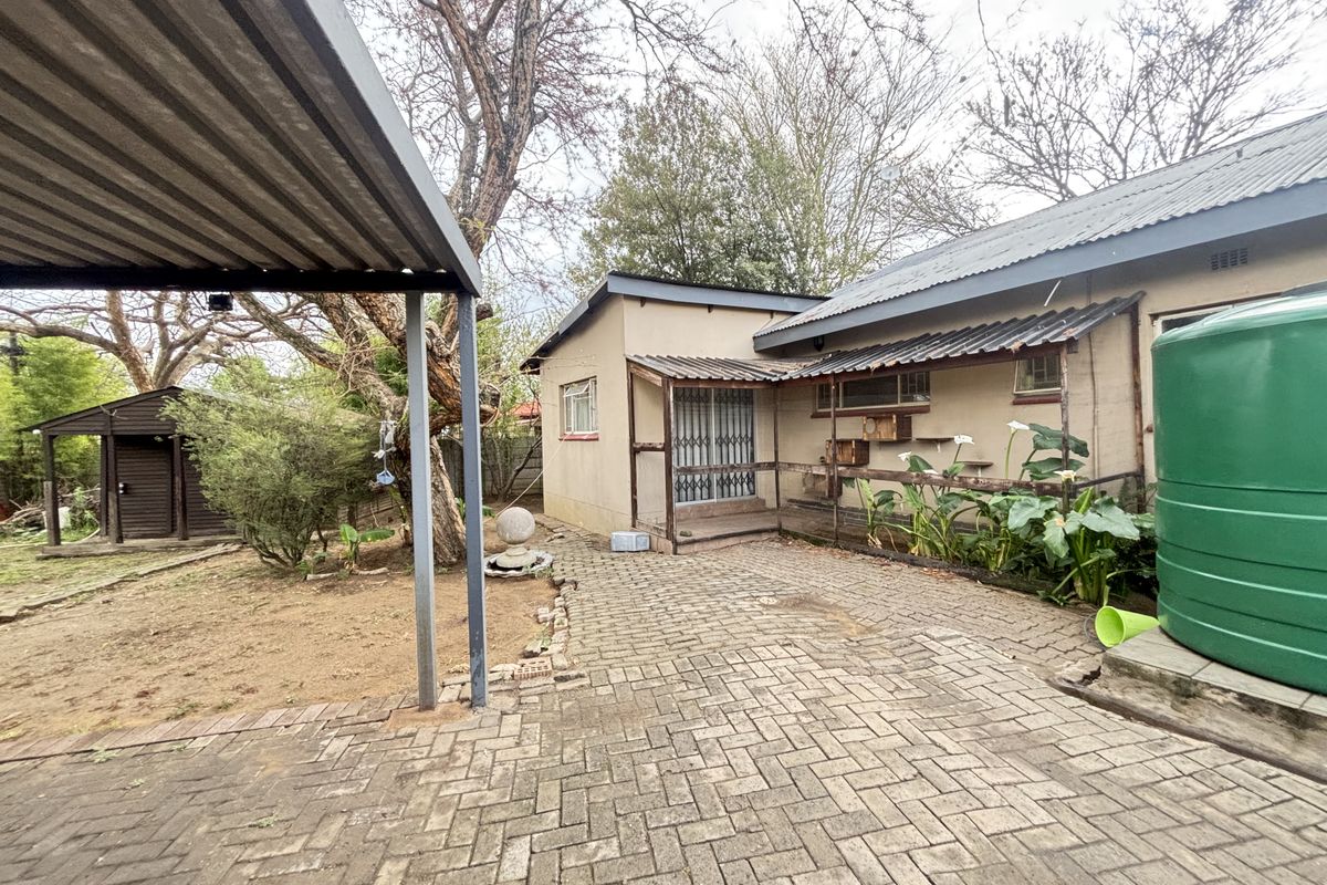 Rear exterior view featuring a paved courtyard, carport, water storage tank, and a small wooden shed in the garden area.