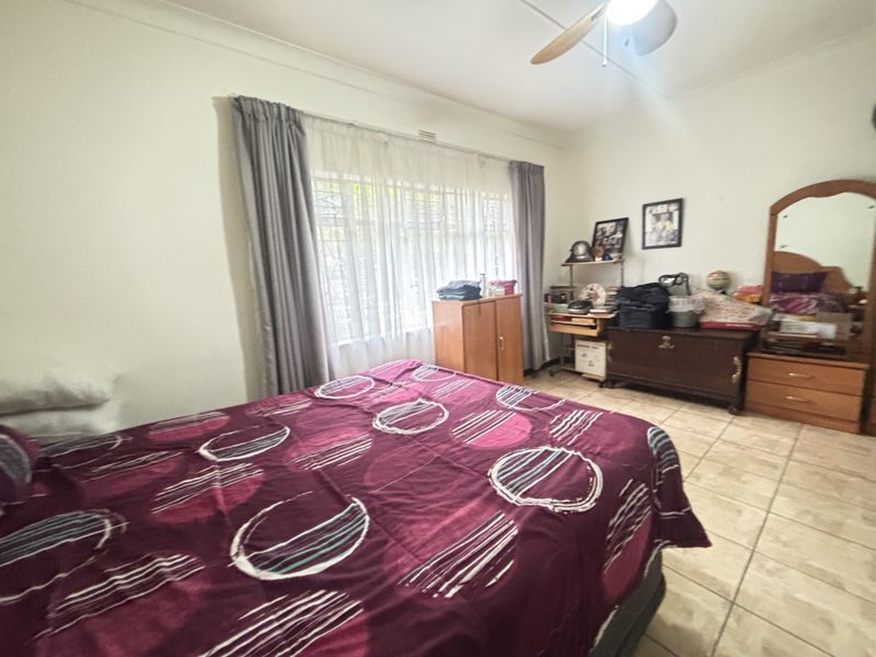 A functional bedroom featuring tiled flooring, a ceiling fan, and large windows fitted with security bars and curtain tracks.