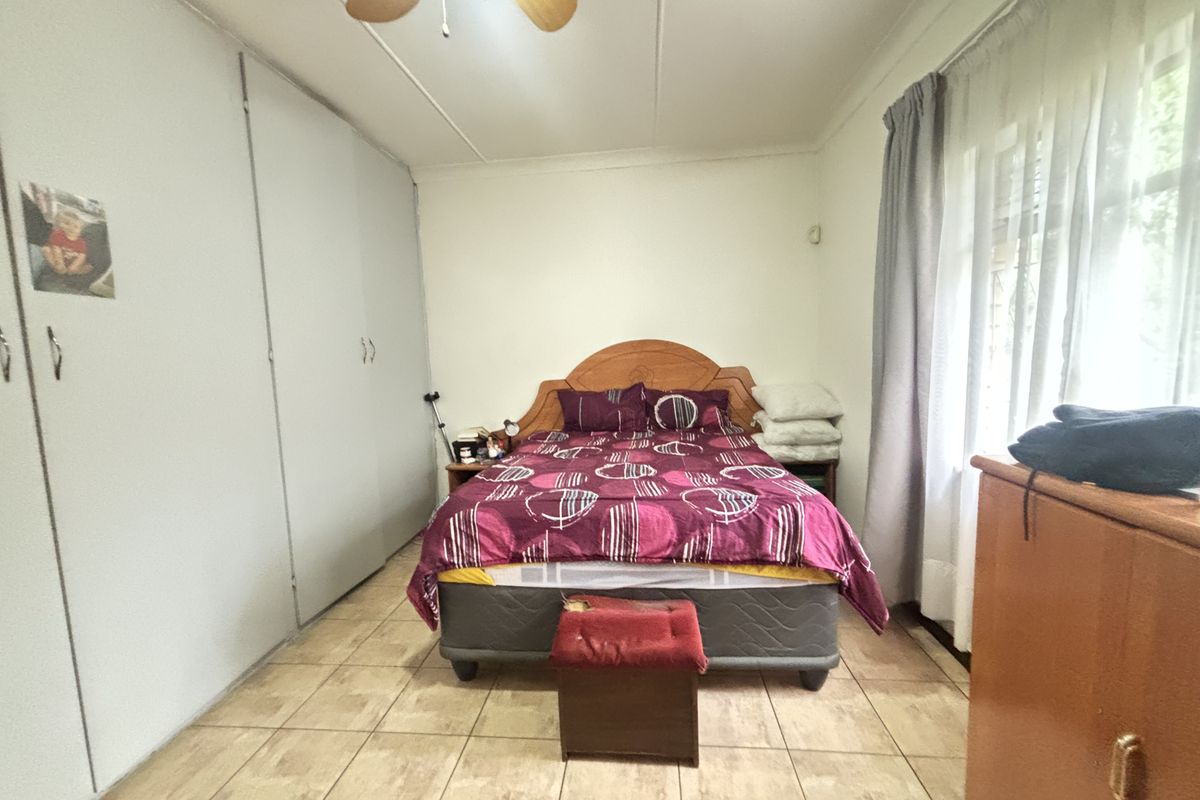 A functional bedroom featuring tiled flooring, built-in cupboards for storage, and a ceiling fan, offering a neutral base for potential updates.