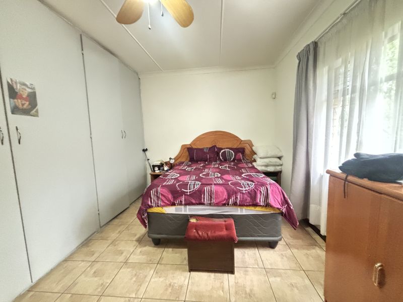 A functional bedroom featuring tiled flooring, built-in cupboards for storage, and a ceiling fan, offering a neutral base for potential updates.