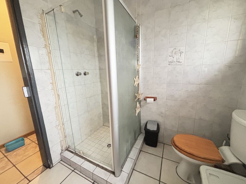 A functional bathroom featuring a corner shower enclosure, toilet, and tiled surfaces. The space shows signs of wear and would benefit from cosmetic updates.