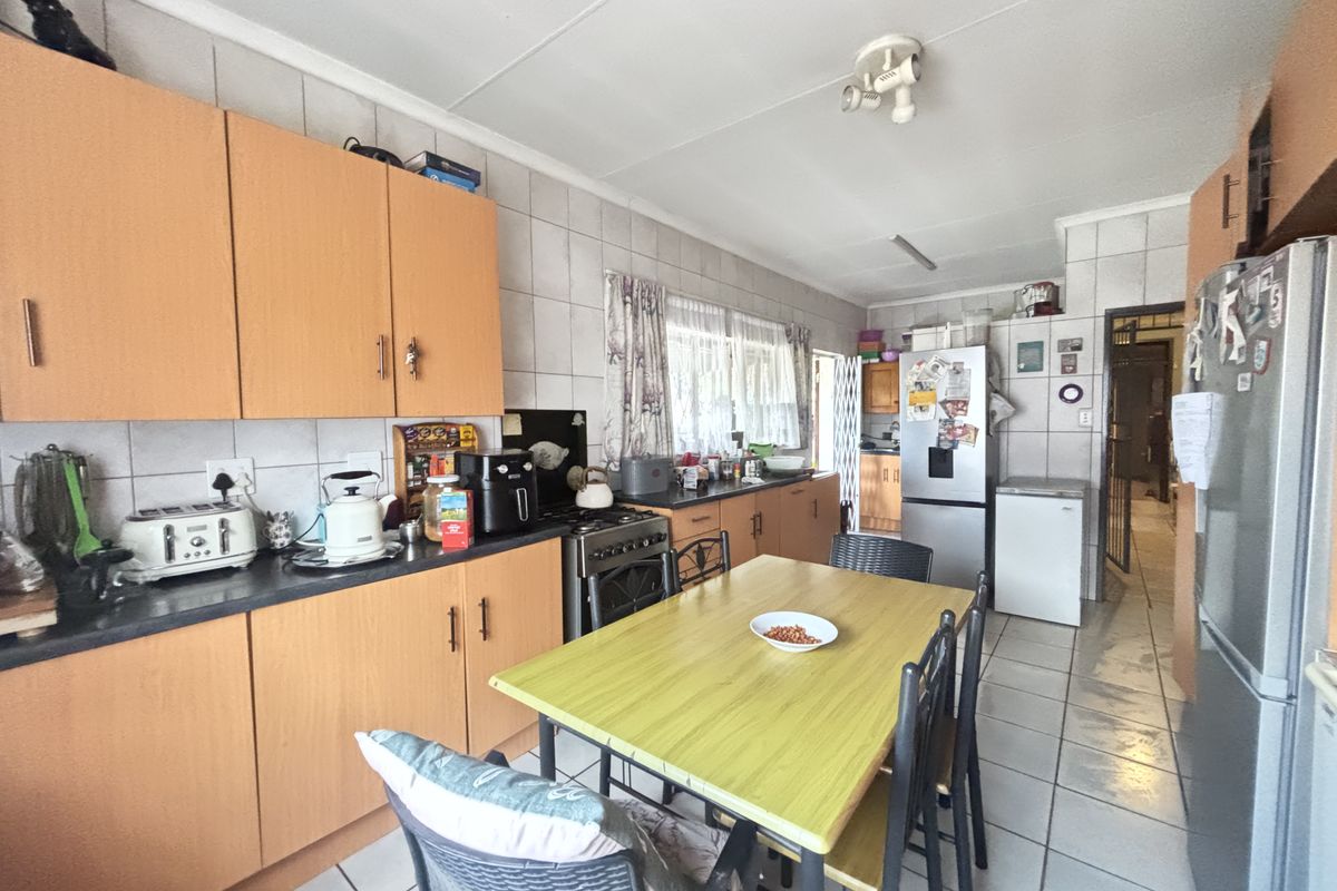 A functional kitchen featuring laminate cabinetry, tiled backsplash, and tiled flooring, offering a practical layout with space for a dining area.