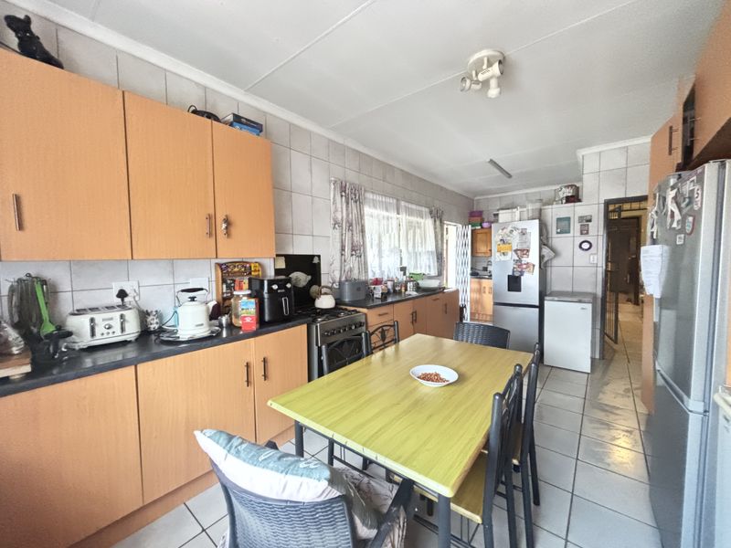 A functional kitchen featuring laminate cabinetry, tiled backsplash, and tiled flooring, offering a practical layout with space for a dining area.