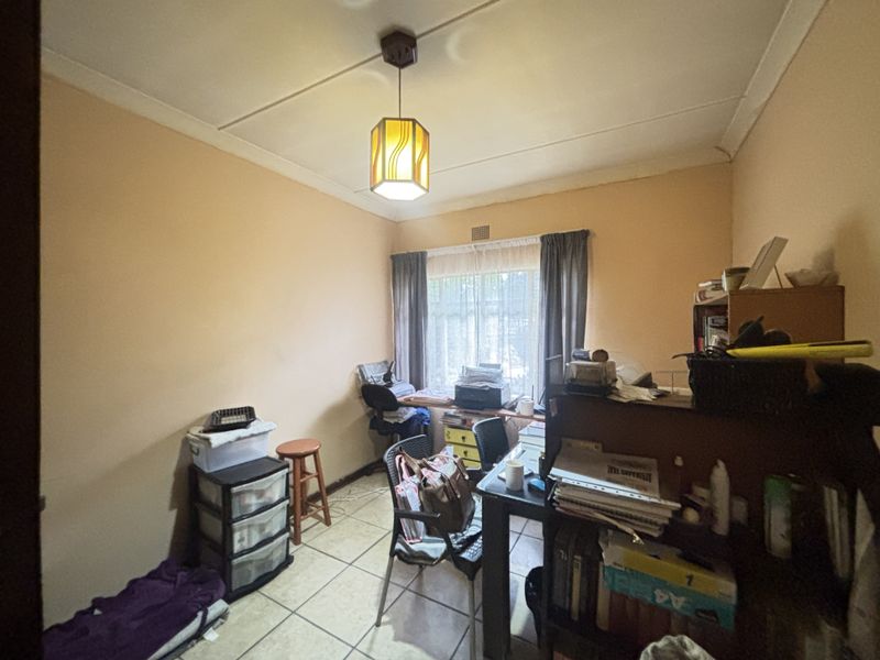 A functional office space featuring tiled flooring and a central pendant light fixture, suitable for a home workspace.
