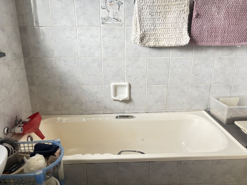 A dated bathroom featuring a built-in bathtub with ceramic wall tiling and a recessed soap dish, showing signs of wear and surface discoloration.