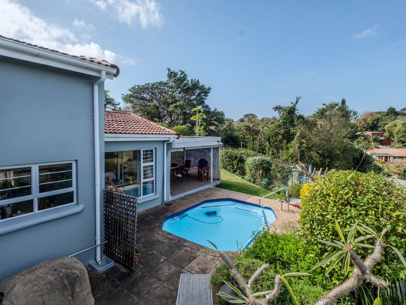 A rear exterior view of the townhouse featuring a swimming pool, paved deck area, and a covered patio space overlooking the garden.