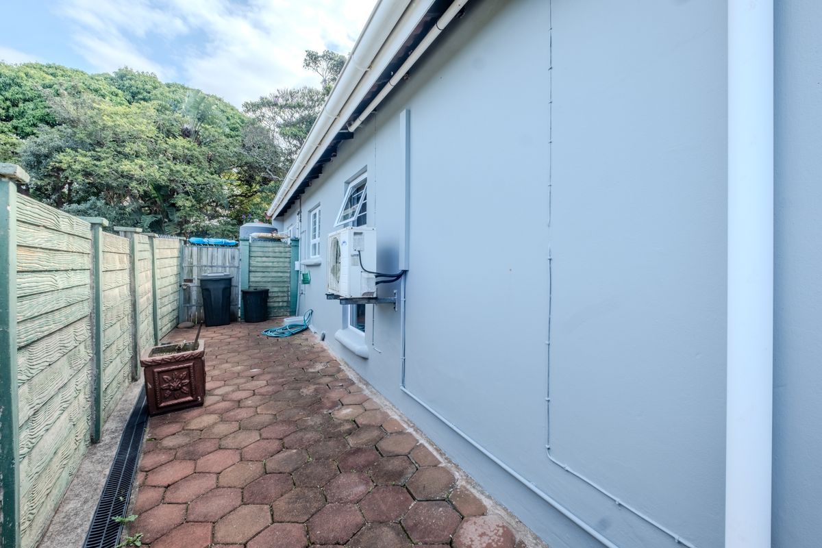 A side exterior view of the townhouse featuring a paved walkway, drainage system, and wall-mounted air conditioning unit.
