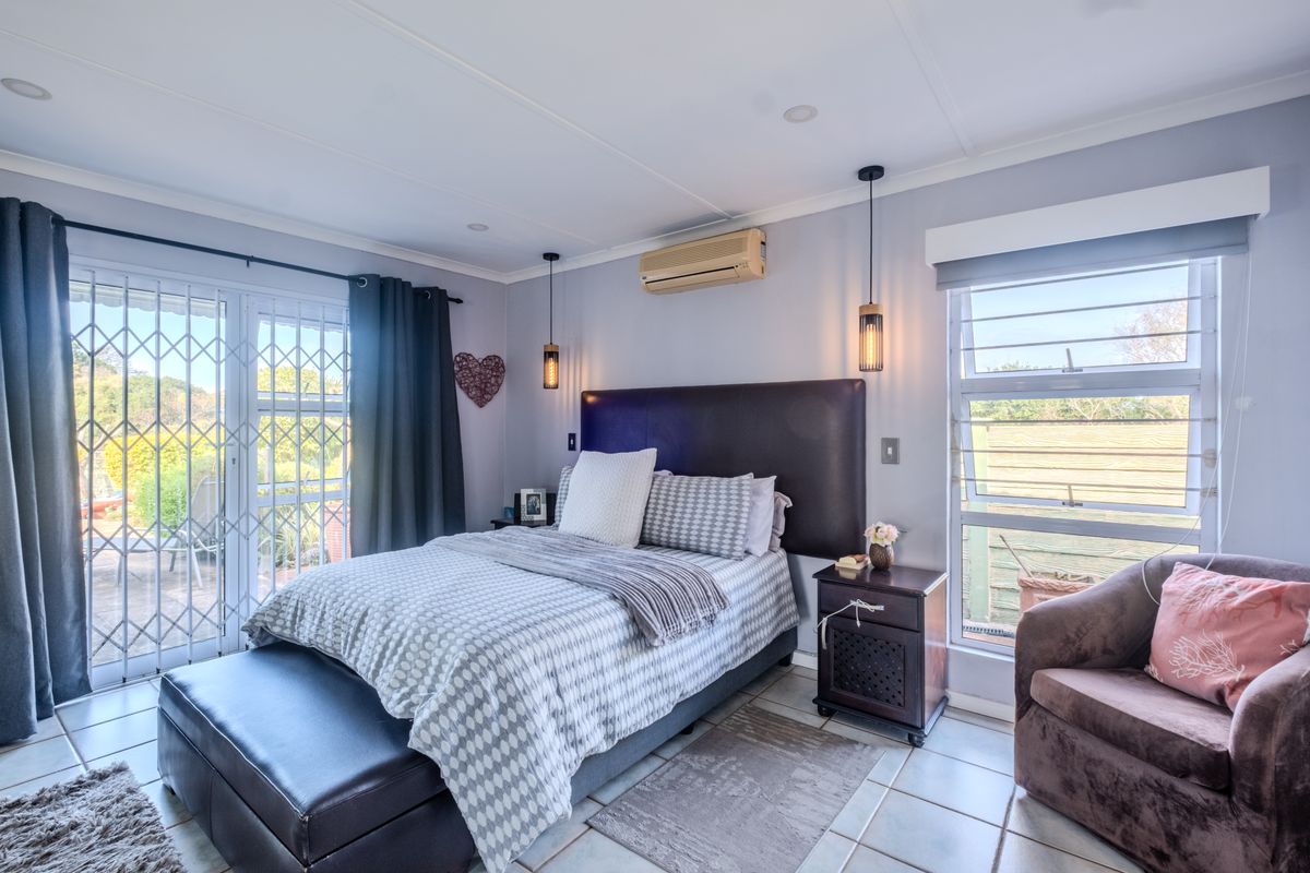 A well-lit bedroom featuring tiled flooring, a split-system air conditioner, pendant lighting, and sliding glass doors with security gates leading to the exterior.