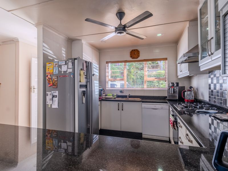 A functional kitchen featuring granite countertops, built-in cabinetry, a gas hob with extractor fan, and a ceiling fan, offering a practical workspace.
