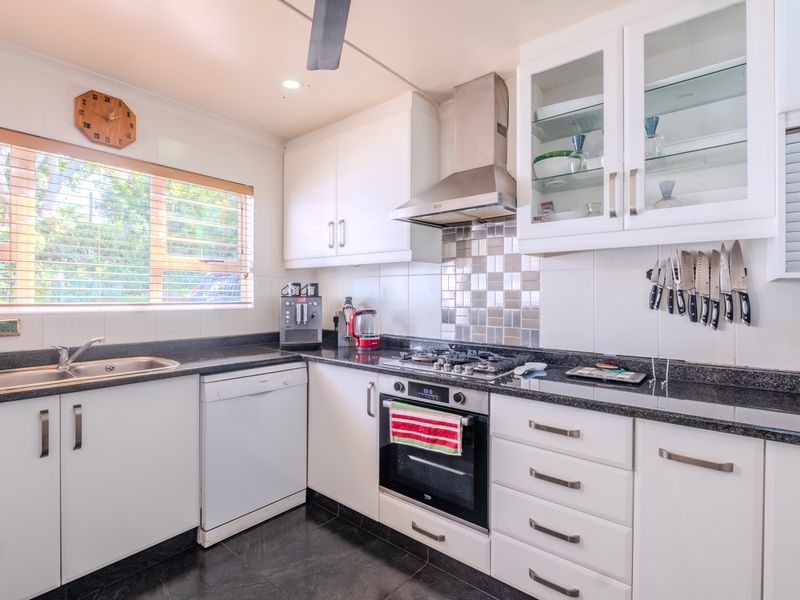 A well-maintained kitchen featuring white cabinetry, granite countertops, a gas hob, built-in oven, and a stainless steel extractor fan.