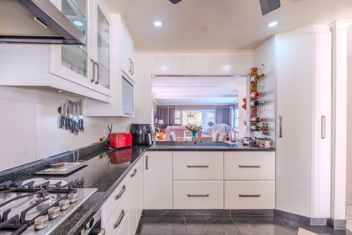 Modern kitchen featuring granite countertops, gas hob, extractor fan, and ample built-in cabinetry, with a convenient pass-through window overlooking the living area.