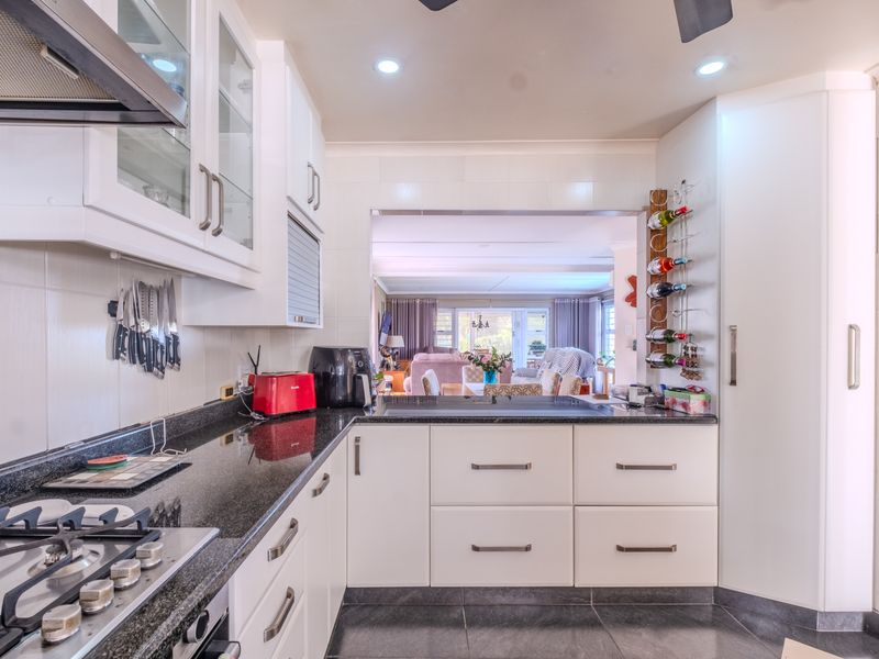 Modern kitchen featuring granite countertops, gas hob, extractor fan, and ample built-in cabinetry, with a convenient pass-through window overlooking the living area.