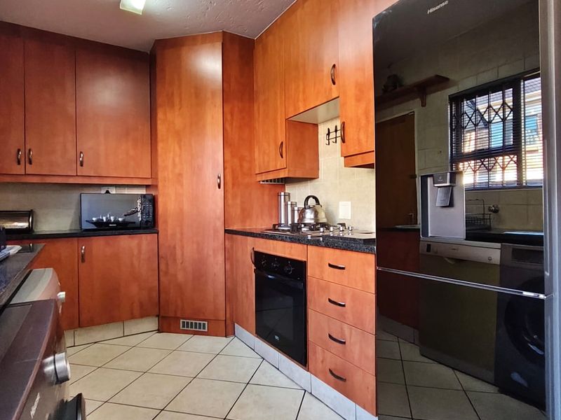 Functional kitchen featuring warm-toned wooden cabinetry, dark laminate countertops, built-in oven, gas hob, and durable ceramic floor tiles.