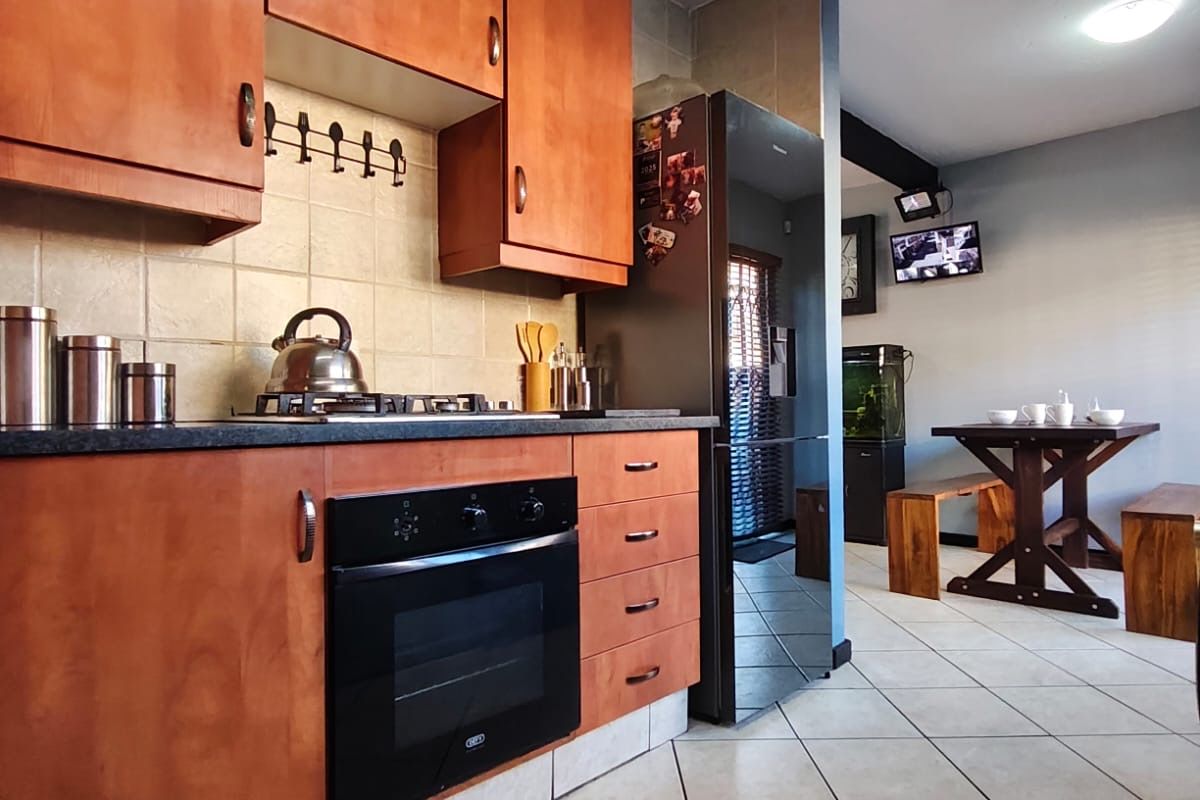 A functional kitchen featuring wooden cabinetry, built-in oven, gas hob, and tiled flooring, flowing into an adjacent dining area.