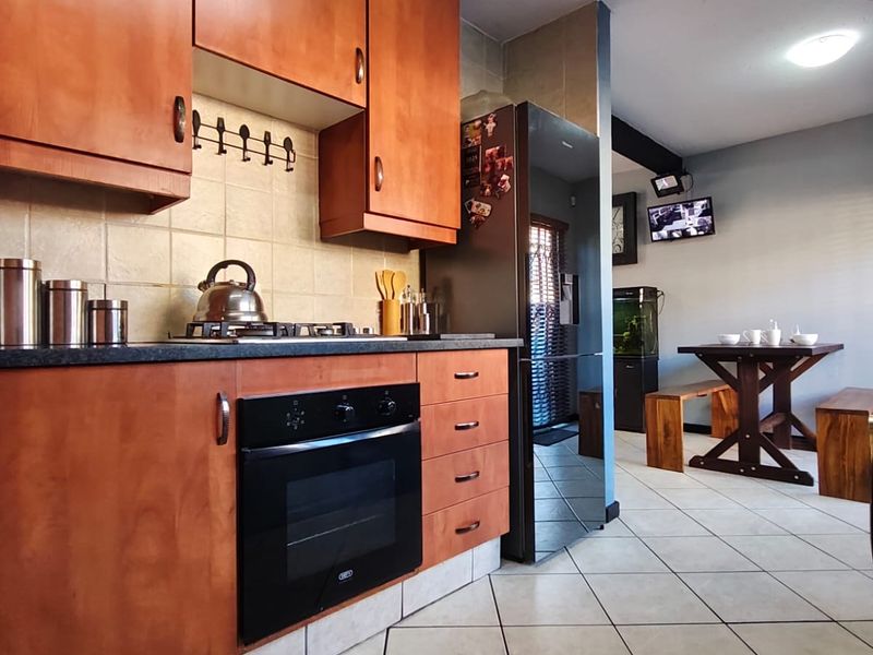 A functional kitchen featuring wooden cabinetry, built-in oven, gas hob, and tiled flooring, flowing into an adjacent dining area.