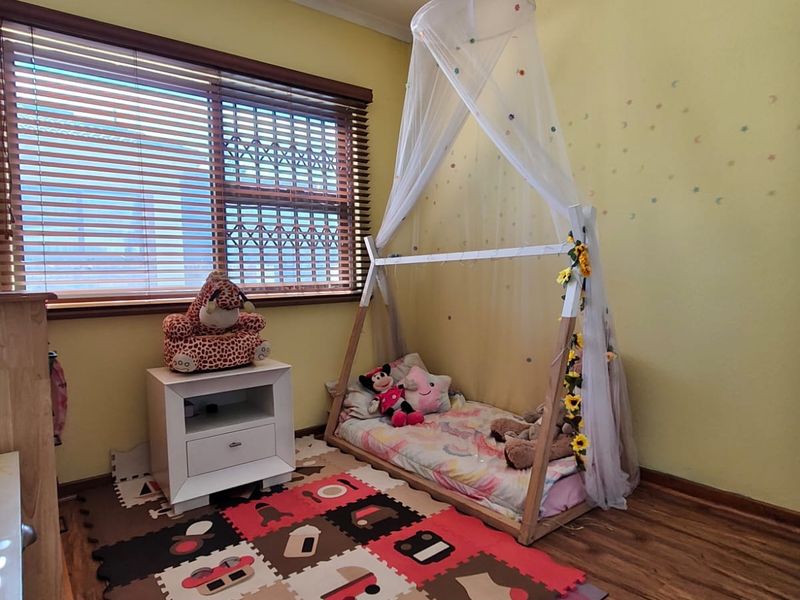 A bedroom featuring timber-look flooring, a ceiling fan, and a window fitted with security bars and timber venetian blinds.