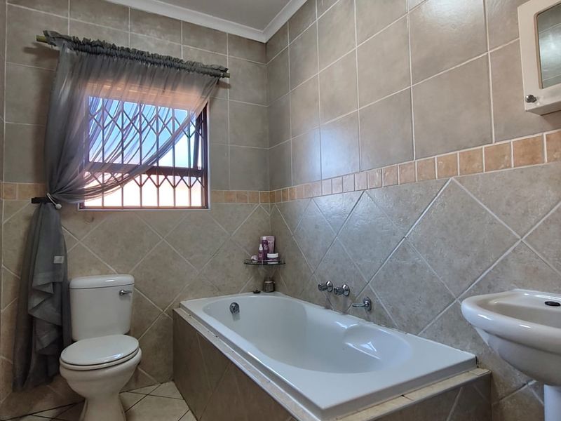 A functional bathroom featuring a built-in bathtub, pedestal basin, toilet, and neutral ceramic tiling throughout.