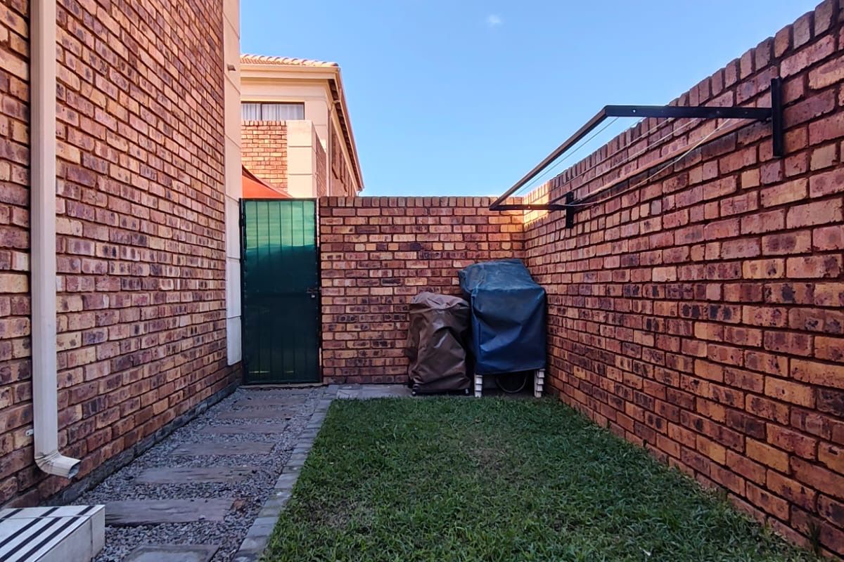 A private rear courtyard featuring brick boundary walls, a small lawn area, paved pathway, and a wall-mounted washing line.
