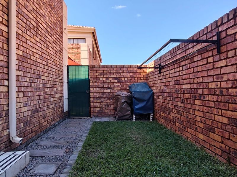 A private rear courtyard featuring brick boundary walls, a small lawn area, paved pathway, and a wall-mounted washing line.
