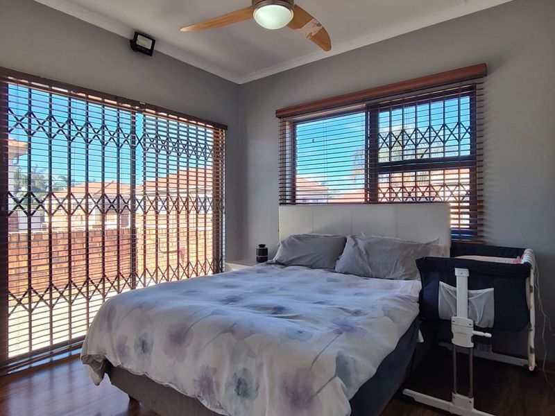 A well-maintained bedroom featuring laminate flooring, a ceiling fan, and secure window and door treatments with fitted venetian blinds.