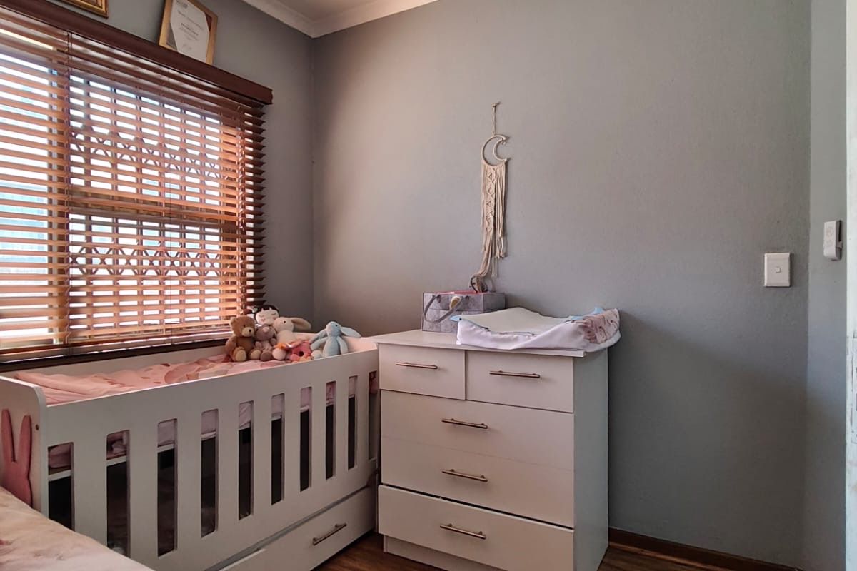 A cozy bedroom featuring laminate flooring, a ceiling fan, and wooden blinds, providing a comfortable and functional living space.