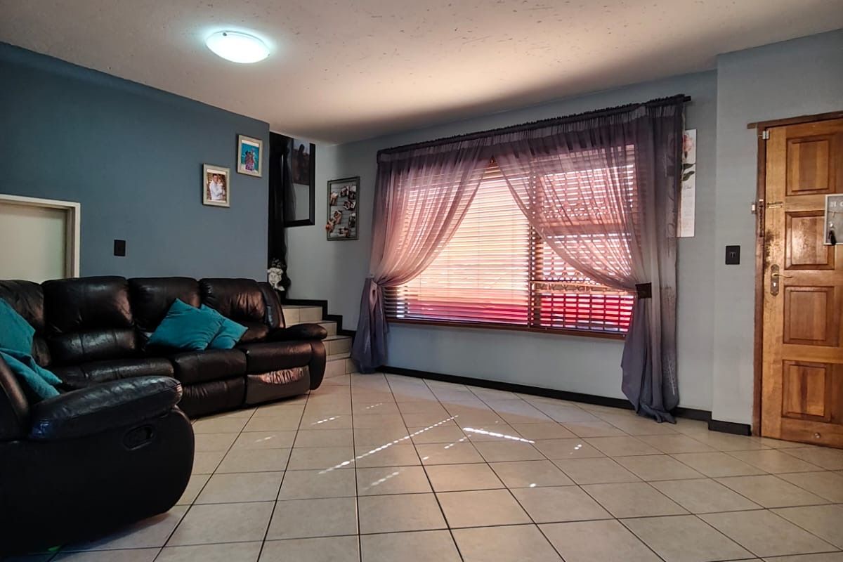 A spacious living room featuring neutral tiled flooring, flush mount ceiling lighting, and a large window with integrated blinds, providing a functional living space.