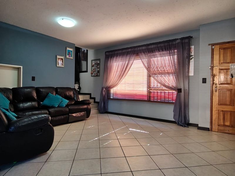 A spacious living room featuring neutral tiled flooring, flush mount ceiling lighting, and a large window with integrated blinds, providing a functional living space.