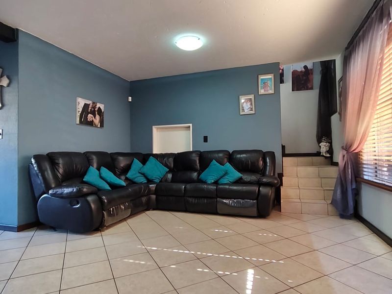 A spacious living room featuring tiled flooring, blue accent walls, and an integrated staircase leading to the upper level.