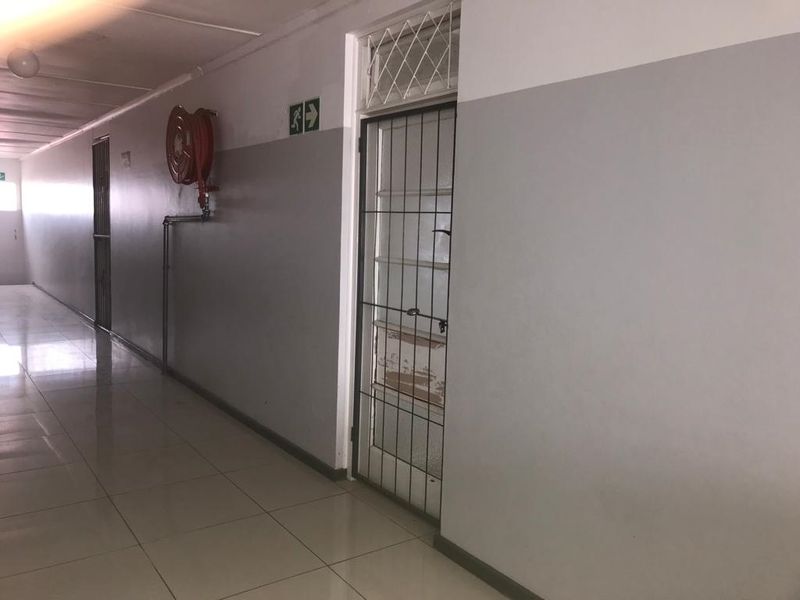 A functional apartment building hallway featuring tiled floors, a wall-mounted fire hose reel, and secure metal entrance gates.
