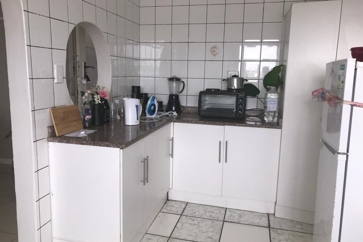 A compact kitchen featuring white cabinetry, granite countertops, and a distinctive circular wall cutout, finished with tiled walls and flooring.