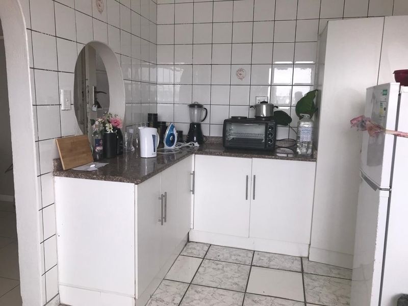 A compact kitchen featuring white cabinetry, granite countertops, and a distinctive circular wall cutout, finished with tiled walls and flooring.