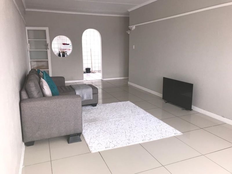 A spacious living room featuring neutral tiled flooring, an arched doorway leading to an adjacent area, and a unique circular window detail.
