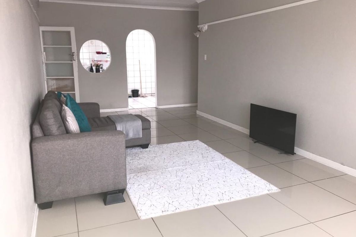 A spacious living room featuring neutral tiled flooring, an arched doorway leading to an adjacent area, and a unique circular window detail.