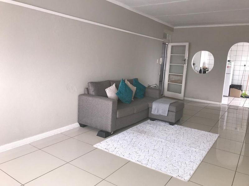 Open plan living area featuring neutral tiled flooring, a classic archway leading to the kitchen, and a glass panel door.