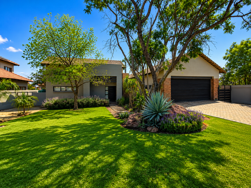 A well-maintained front elevation featuring a paved driveway, double garage, and beautifully landscaped garden with mature trees and established planting.
