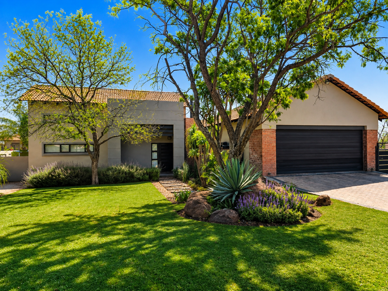 Attractive front elevation featuring a well-maintained garden, paved driveway, double garage, and a modern entrance with tiled roof detailing.
