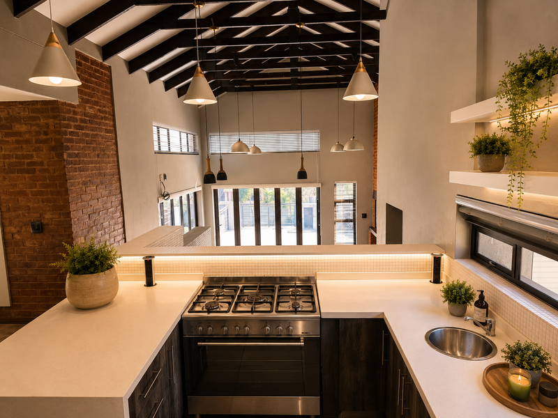 Modern open-plan kitchen featuring stone countertops, a gas cooktop, and exposed timber beams, overlooking a bright living area with large stacking glass doors.